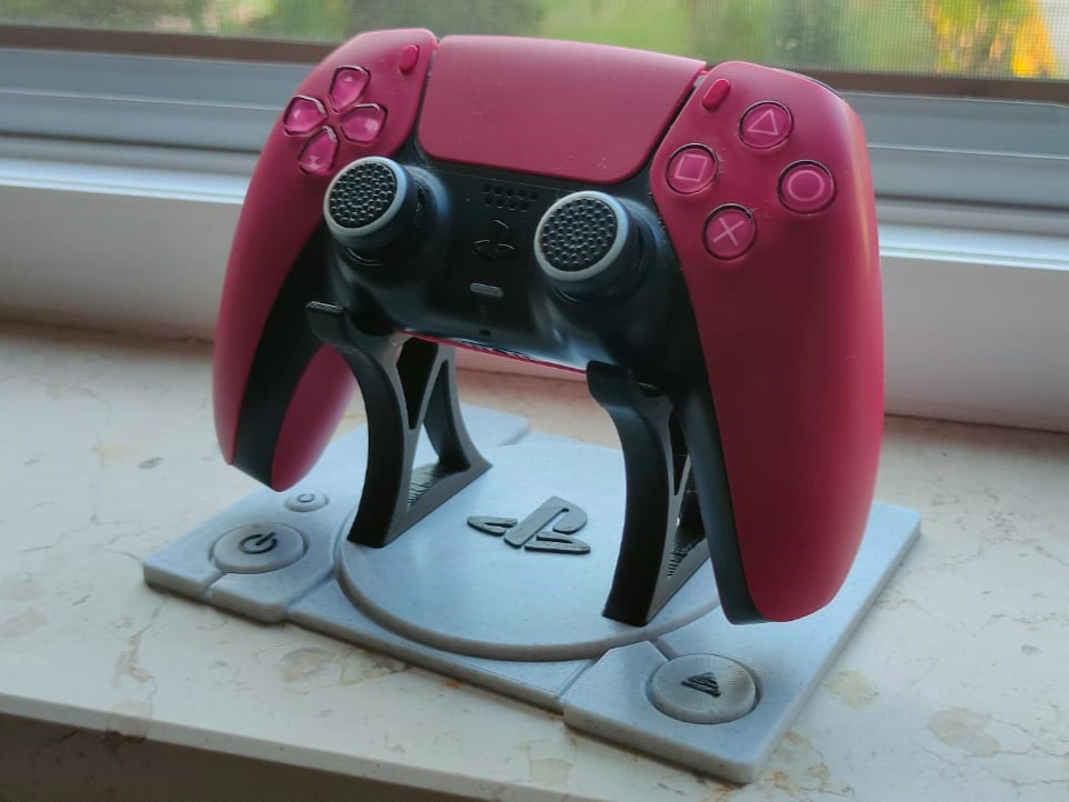 Pink DualSense controller on a grey 3D-printed stand styled like a PlayStation 1 console top