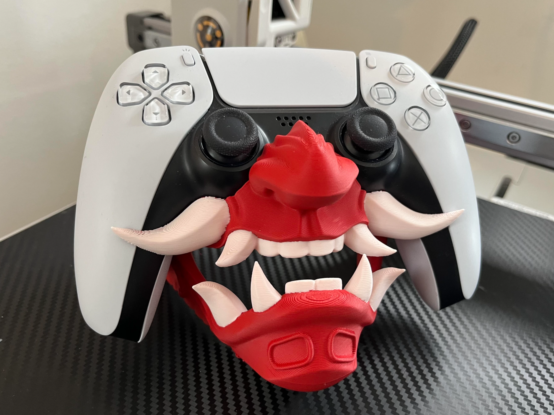 White DualSense controller with red 3D-printed oni mask accessory under the analog sticks