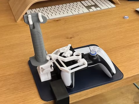 DualSense controller with grey 3D-printed flight joystick attachment and desk clamp on a wooden desk