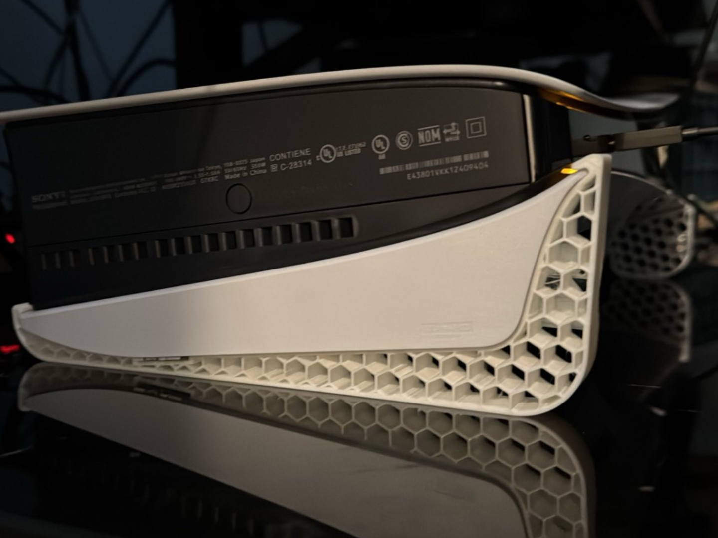 PlayStation 5 console on a white 3D-printed honeycomb horizontal stand on a dark reflective surface