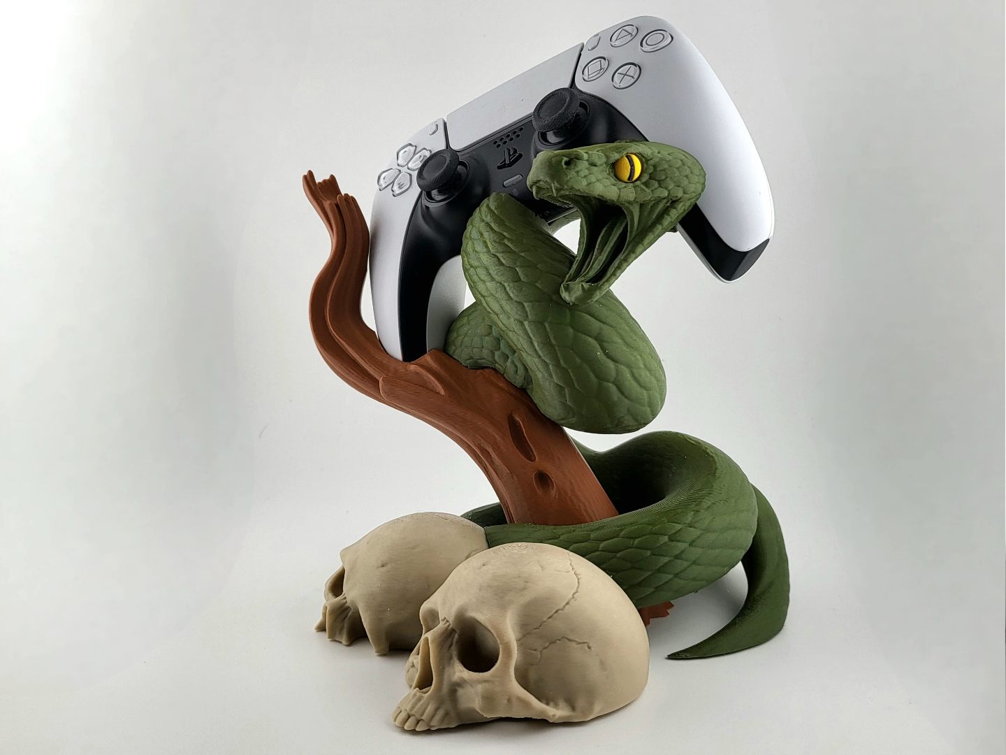 3D-printed stand with green snake, tree branch, and skulls holding a white and black PS5 DualSense controller